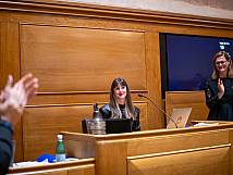 Stadtratspräsidentin Valentina Achermann sitzt auf ihrem Platz und bekommt stehenden Applaus vom Stadtrat. Rechts im Bild Ratssekretärin Nadja Bischoff.